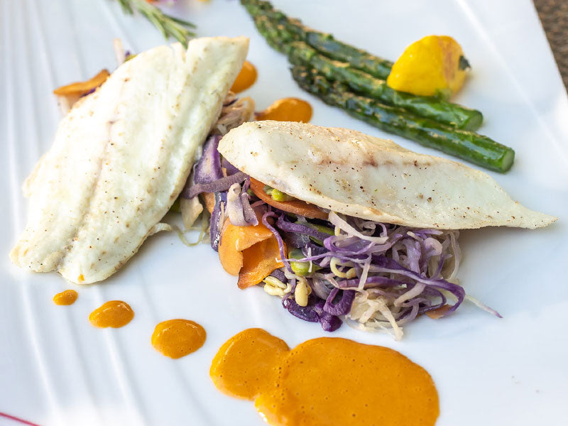 Filets de poisson avec légumes et sauce, disposés sur une assiette élégante.
