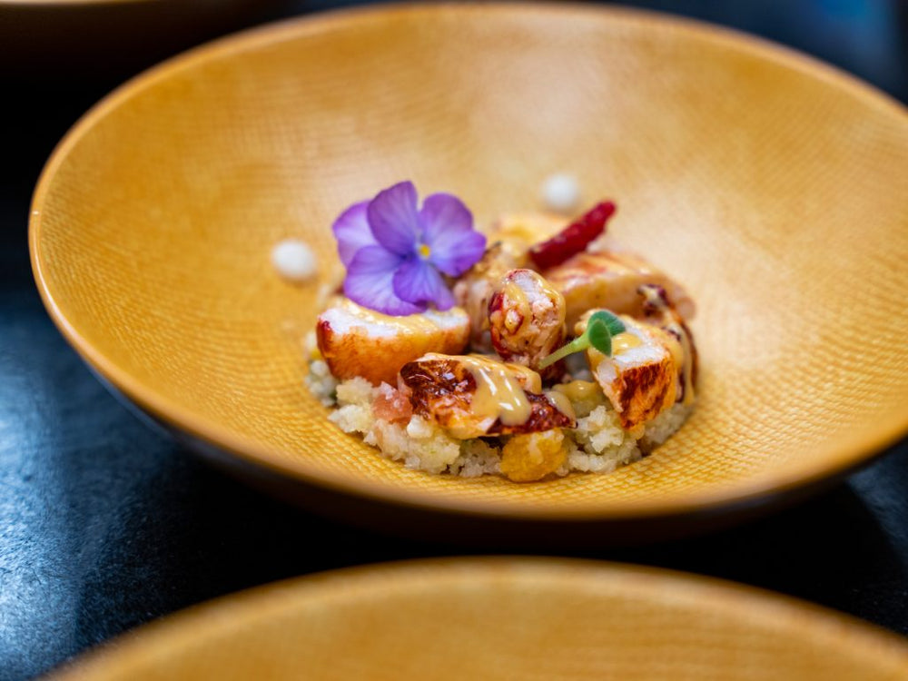 Un plat gastronomique avec des morceaux de homard délicatement disposés sur une semoule fine, décoré d'une fleur comestible.