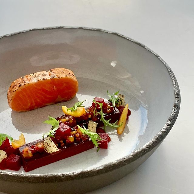 Plat gastronomique composé d'un filet de saumon légèrement saisi, accompagné de légumes colorés et d'une présentation artistique dans une assiette en céramique élégante.