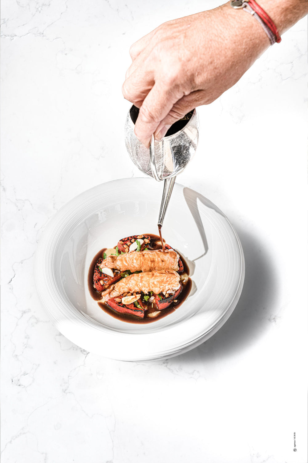 Main versant une sauce sur un plat raffiné composé de fruits de mer dans une assiette blanche.
