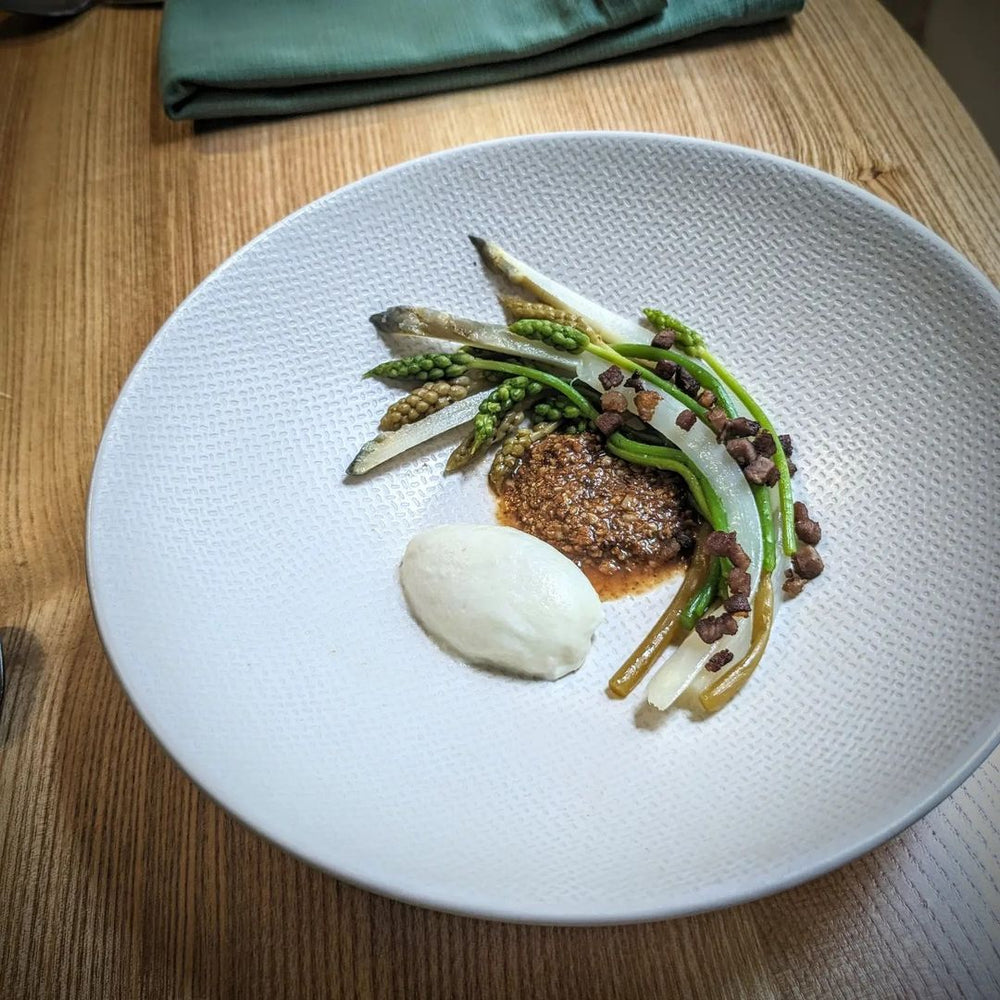 Assiette gastronomique avec légumes verts et purée, présentée sur une table en bois.
