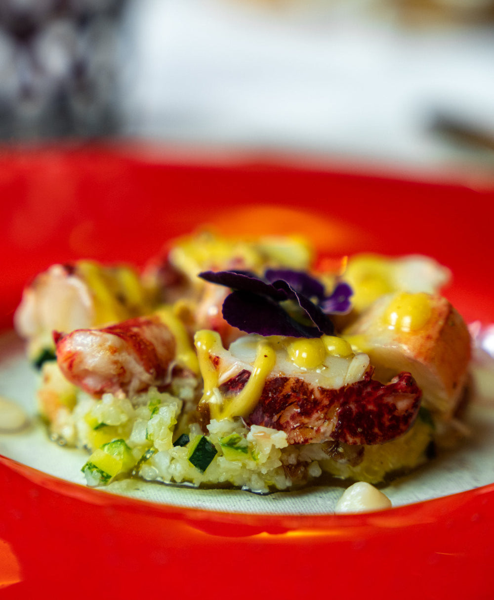 Un autre plat de homard soigneusement dressé avec des légumes frais et une sauce onctueuse, servi sur une assiette rouge vibrante.