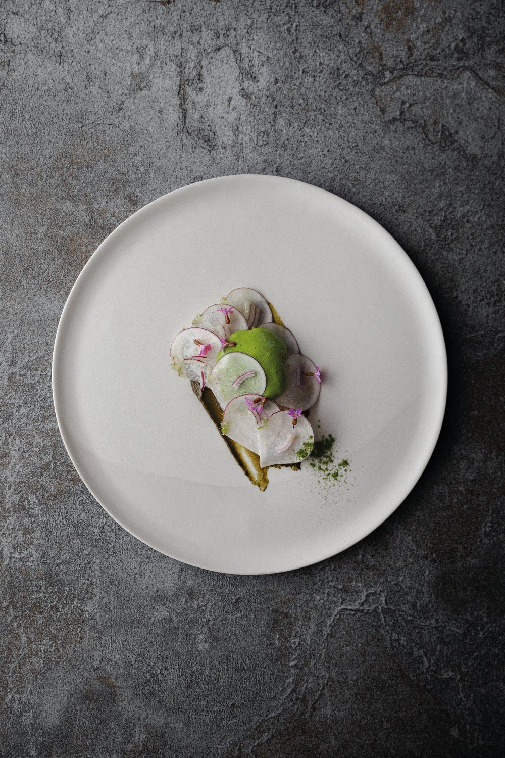 Assiette gastronomique élégante avec des tranches fines de radis et une quenelle verte, soigneusement disposées sur une assiette blanche minimaliste.
