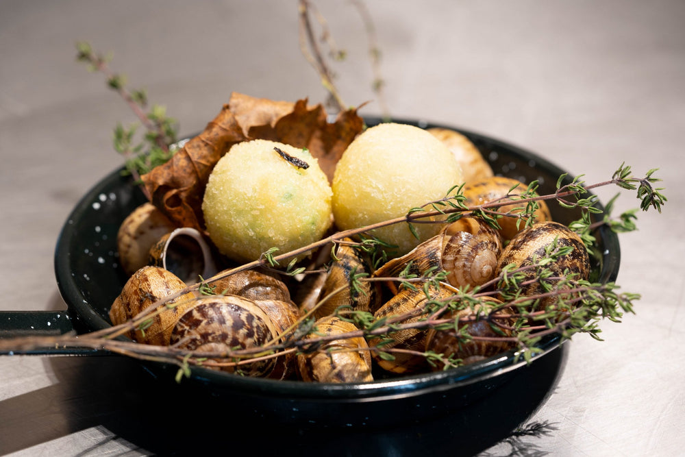 Escargots servis dans une casserole noire avec des herbes fraîches et des boulettes croustillantes.