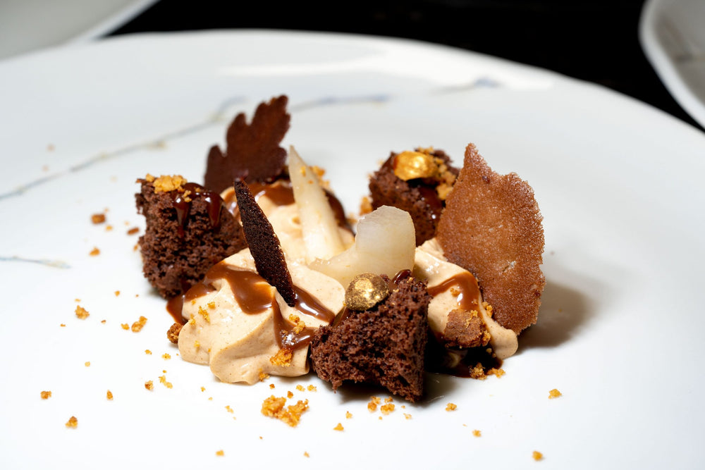 Dessert gourmet au chocolat avec des décorations dorées et des morceaux de biscuits croquants.