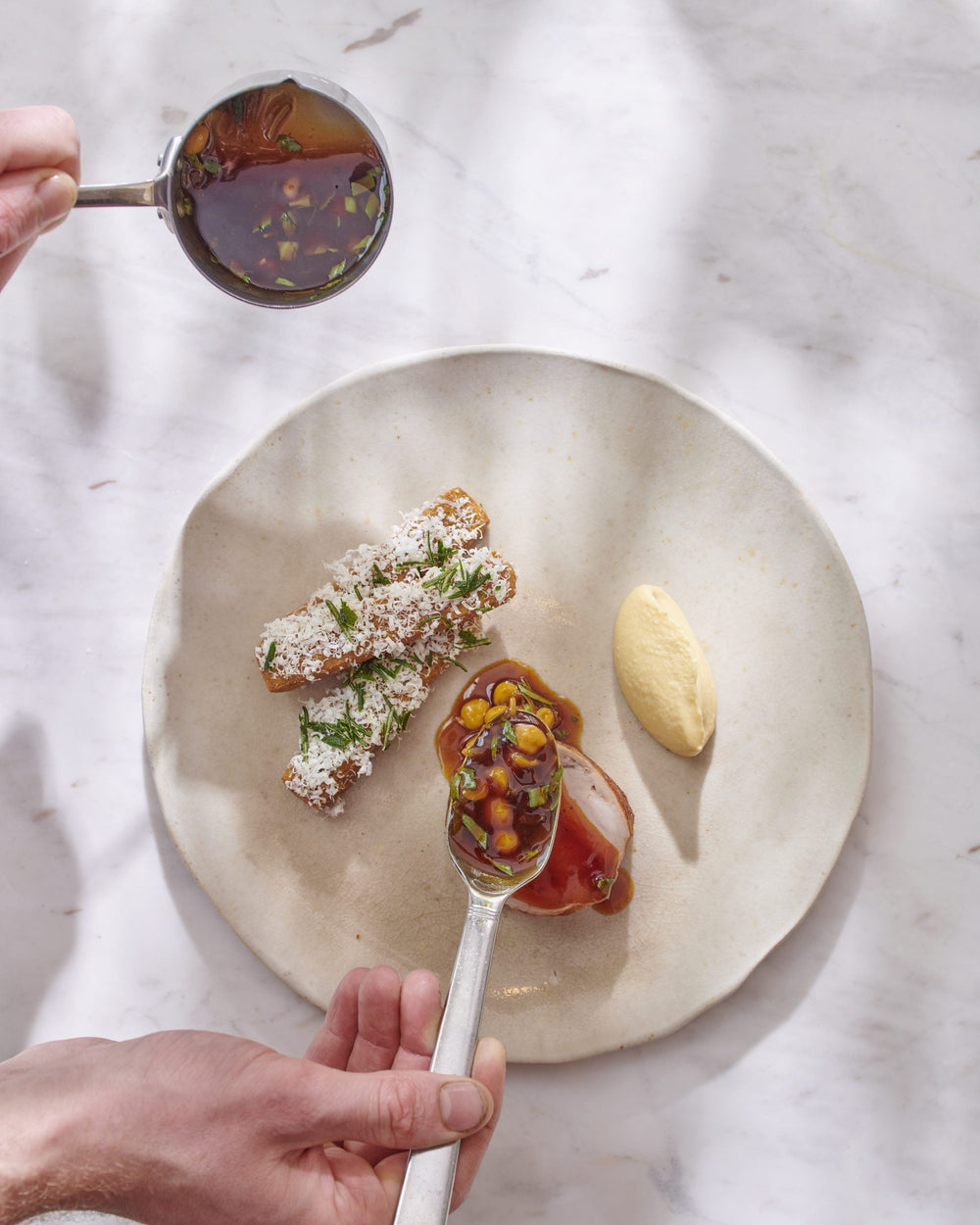 Main versant une sauce sur un plat composé de viande, de légumes et d'une purée blanche.
