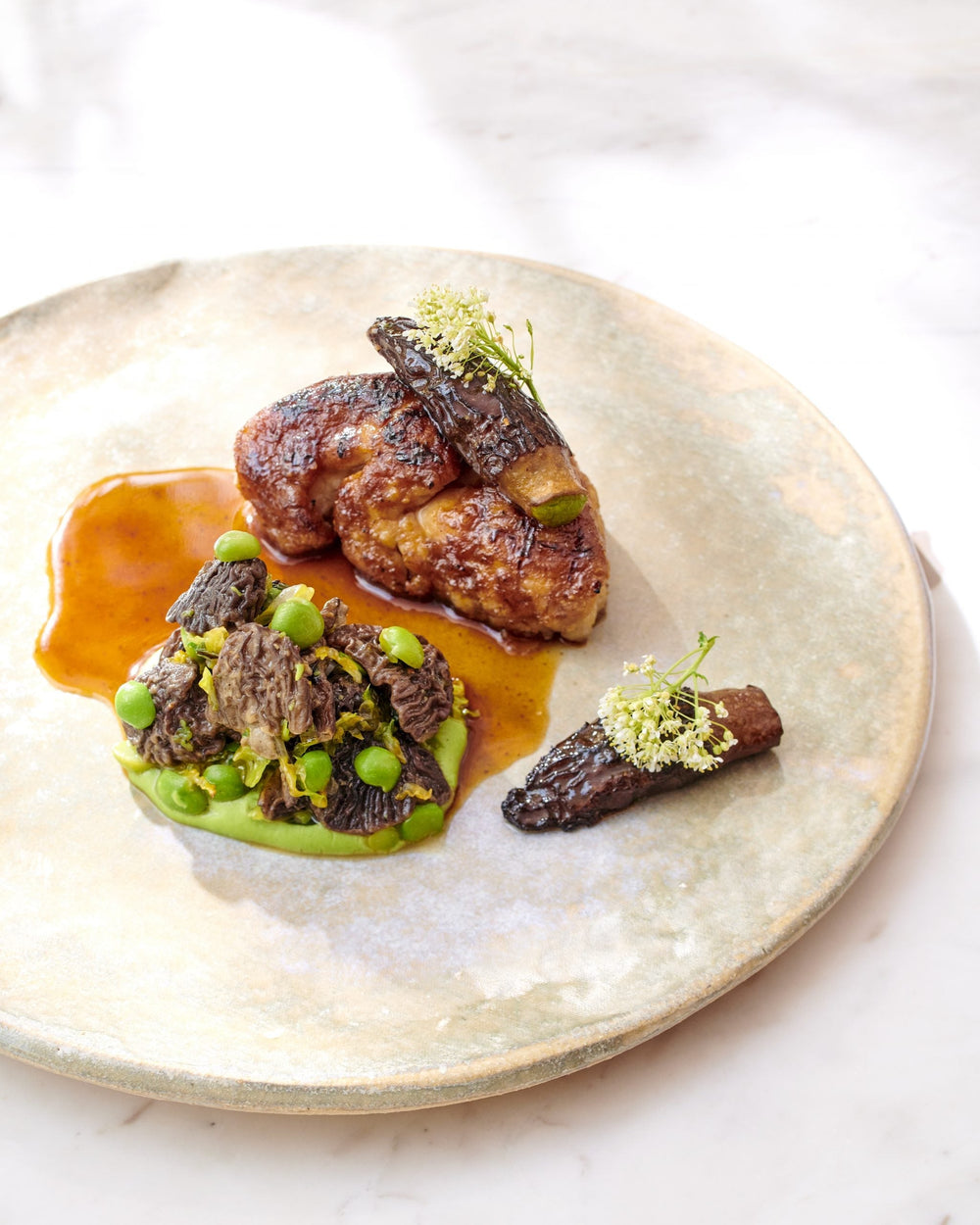 Plat de viande avec des morilles, des petits pois et une sauce, présenté de manière artistique.