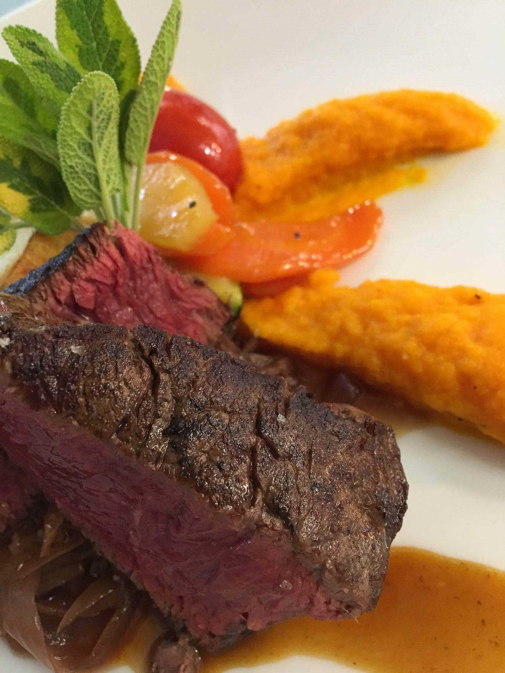 Pièce de viande rouge grillée accompagnée de purée de carottes et légumes colorés, garnie d'herbes fraîches.







