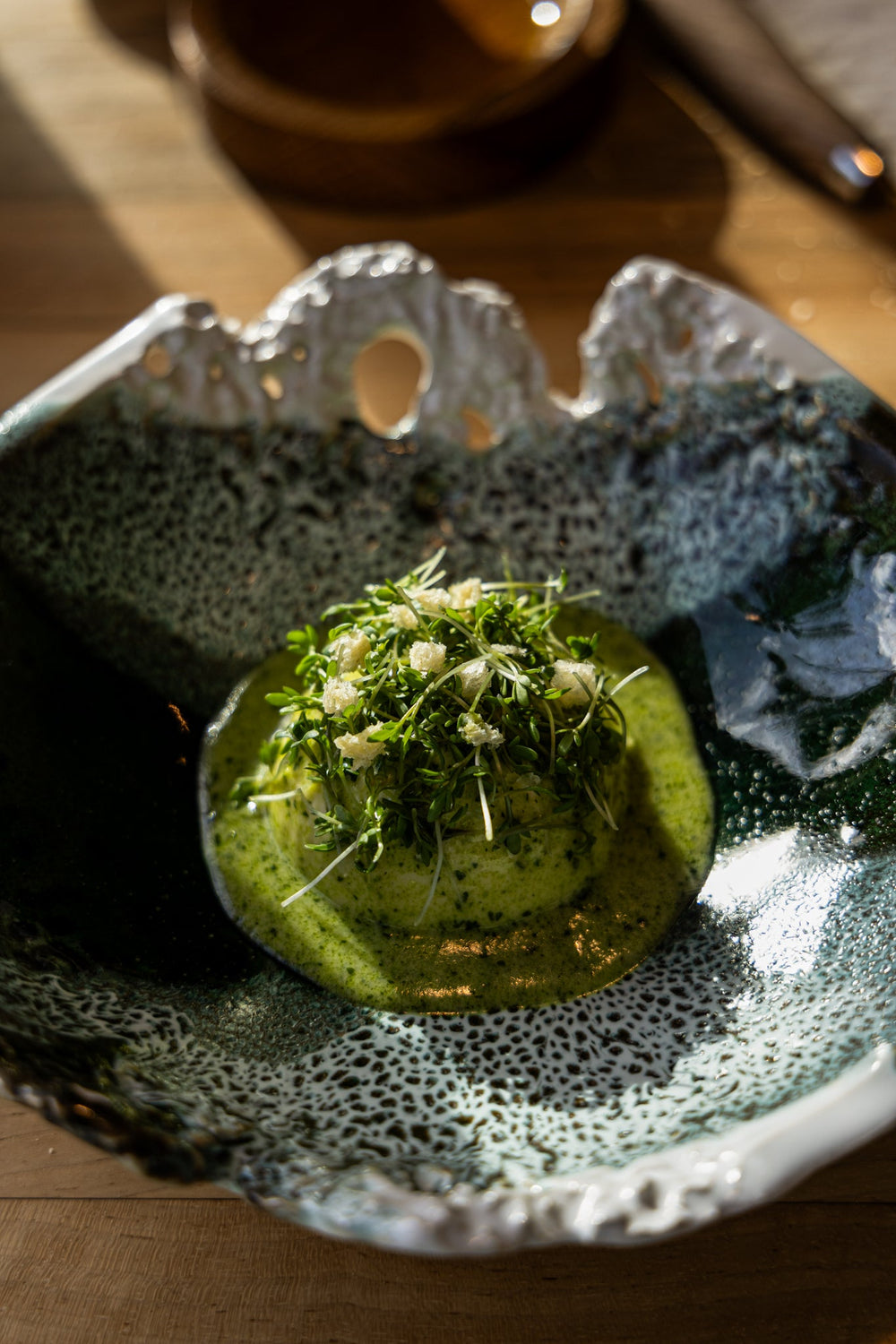 Plat gastronomique dans une assiette en céramique artistique, garni de légumes verts frais et de sauce verte.