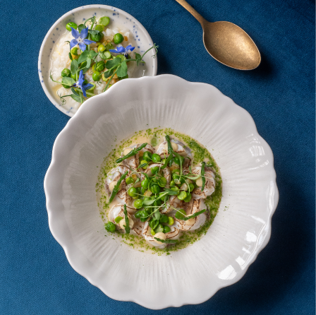 Plat raffiné de fruits de mer et herbes fraîches présenté sur une nappe bleue.
