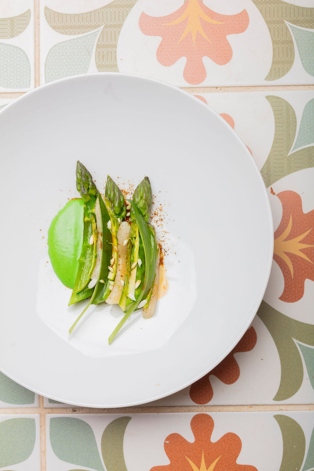 Assiette blanche avec des asperges vertes artistiquement disposées et une sauce verte sur le côté.