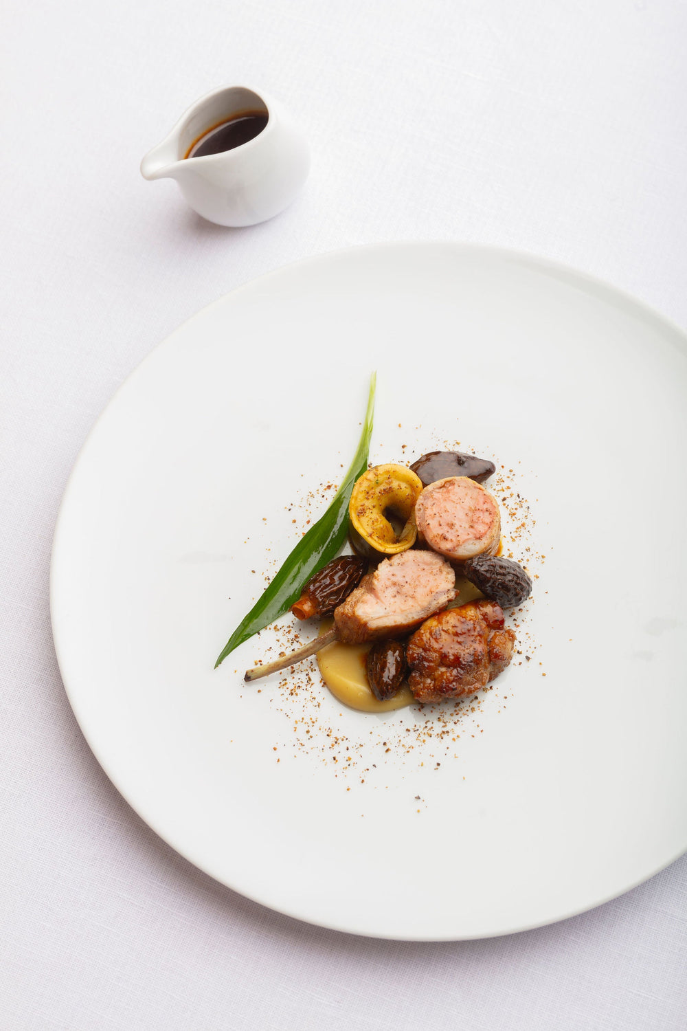 Plat gastronomique composé de morceaux de viande et de légumes, présenté sur une assiette blanche avec une petite sauce en accompagnement.