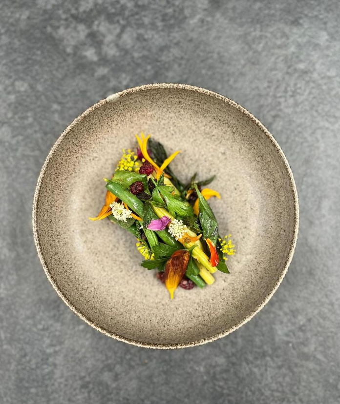Assiette de légumes verts et fleurs comestibles sur une assiette en céramique rustique.
