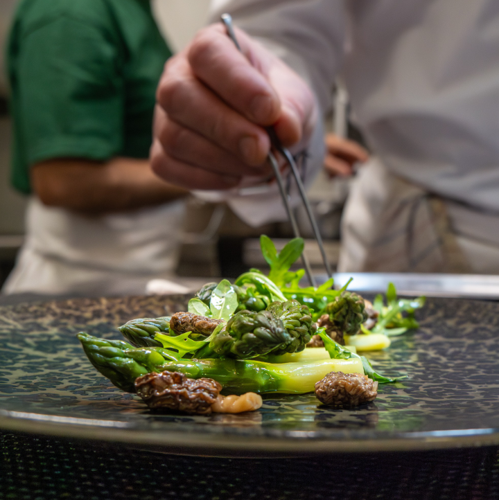 Chef qui ajuste un plat à la pince à épilée avec des asperges, de la roquette et des morilles