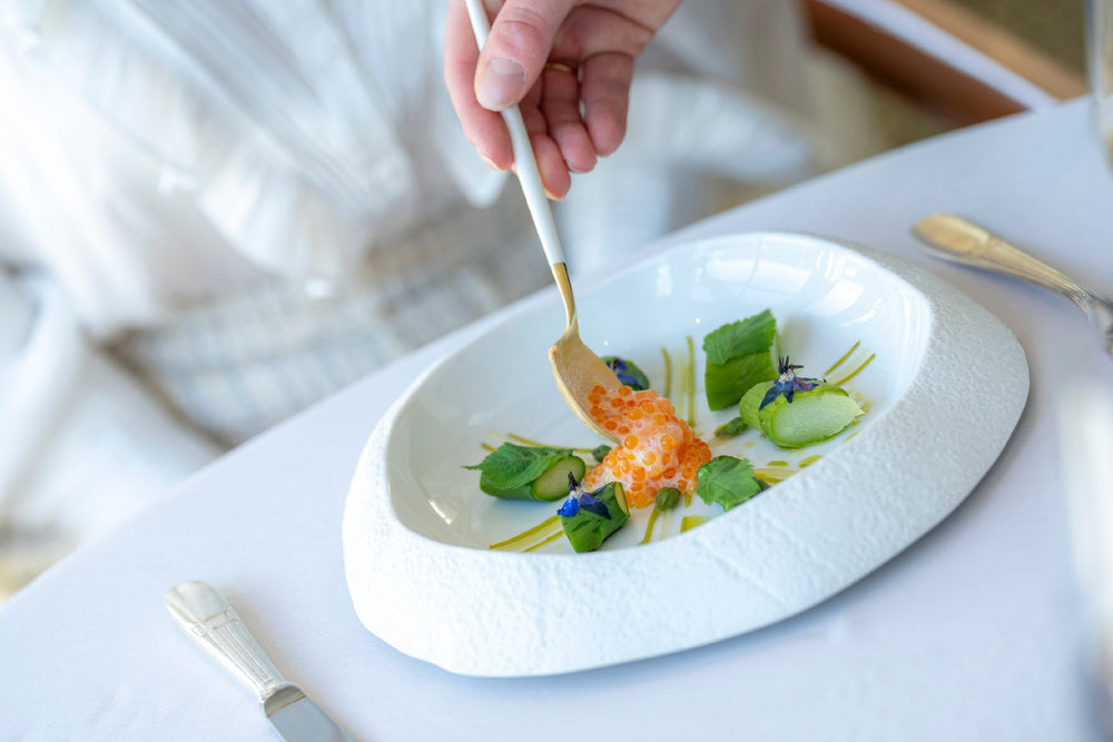 Plat gastronomique avec des perles de saumon, des garnitures vertes et des fleurs comestibles, servi dans une assiette blanche.