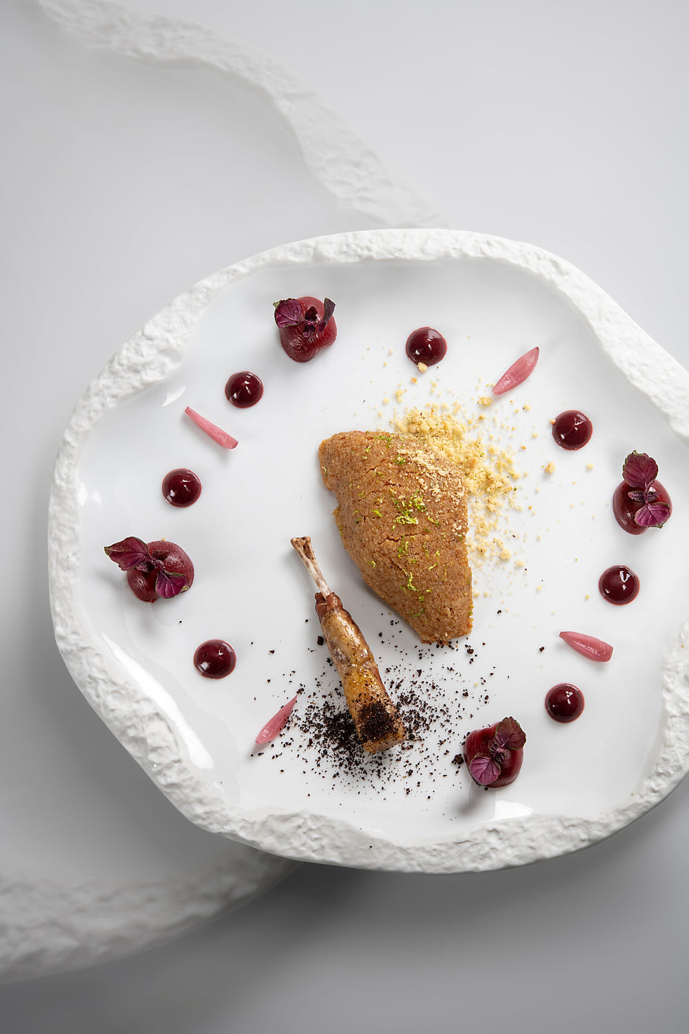 Plat gastronomique disposé artistiquement dans une assiette blanche, avec des garnitures et des sauces colorées.