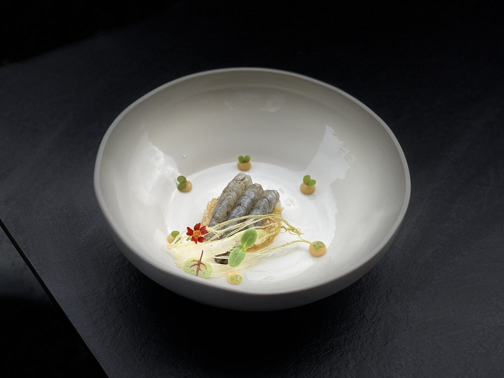 Plat gastronomique dans une assiette blanche avec des gambas et des éléments de décoration artistique.