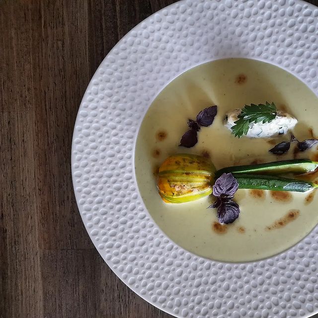 Assiette gastronomique avec courgette fleurie et sauce crémeuse, décorée de feuilles aromatiques.






