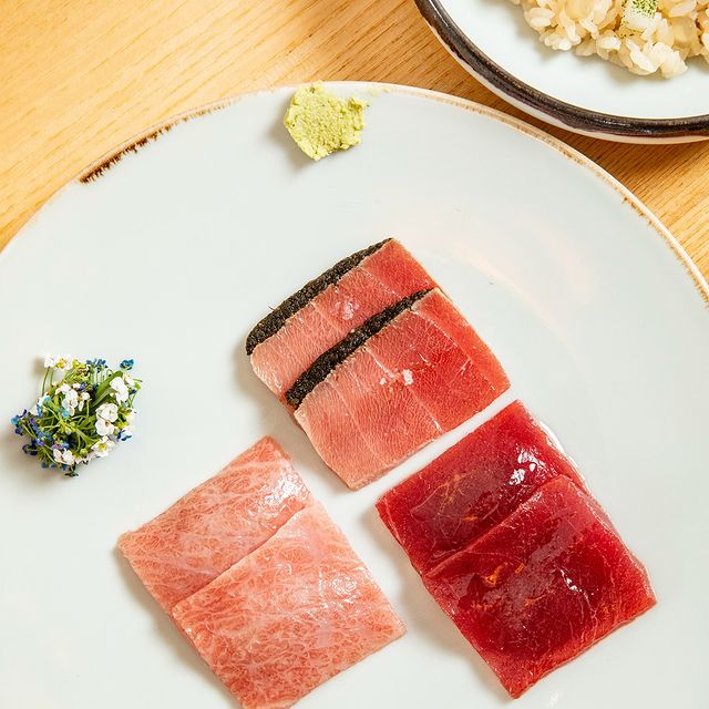 Assiette de sushi avec des tranches de poisson cru, accompagnée de wasabi et de fleurs comestibles.