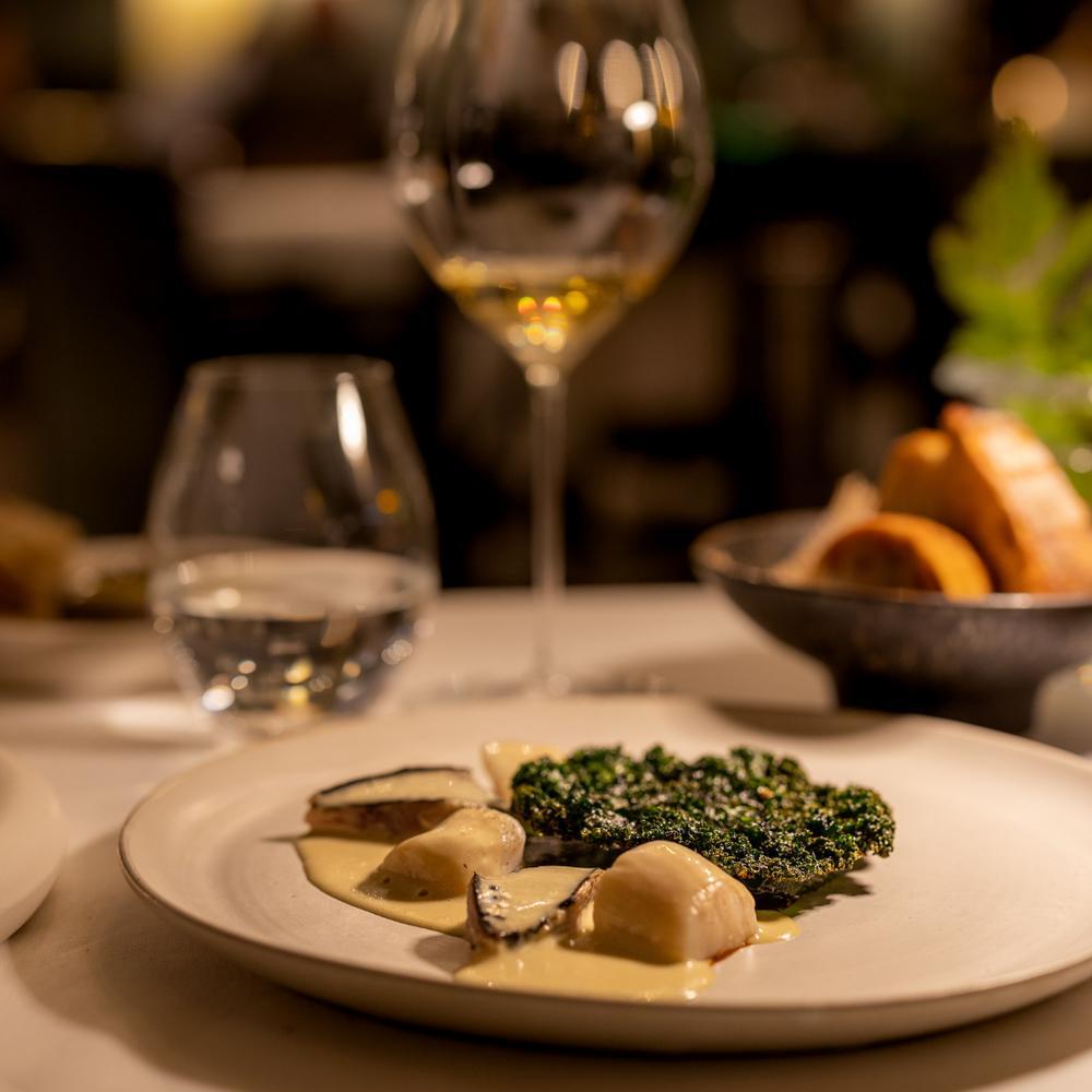 Un plat gastronomique avec des légumes et une sauce crémeuse, accompagné de verres de vin et de pain.