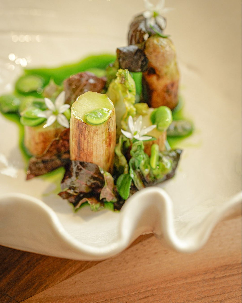 Plat raffiné avec des légumes verts et des fleurs comestibles, présenté dans une assiette blanche aux bords ondulés.